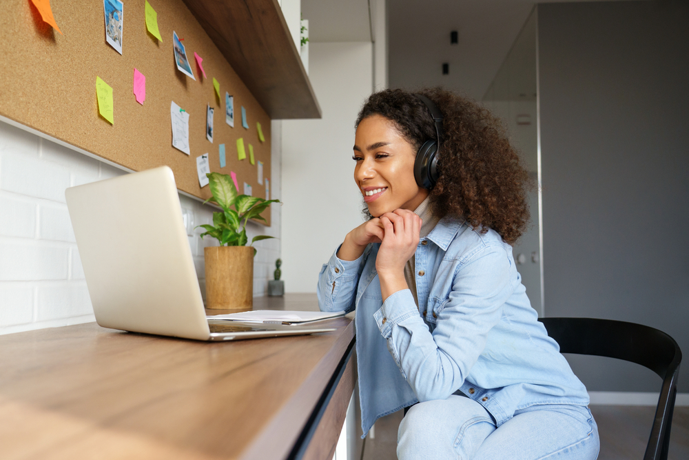 Secrets to Negotiating a Higher Salary for Your Remote Job: Picture of a happy young lady smiling at her laptop while working from home.
