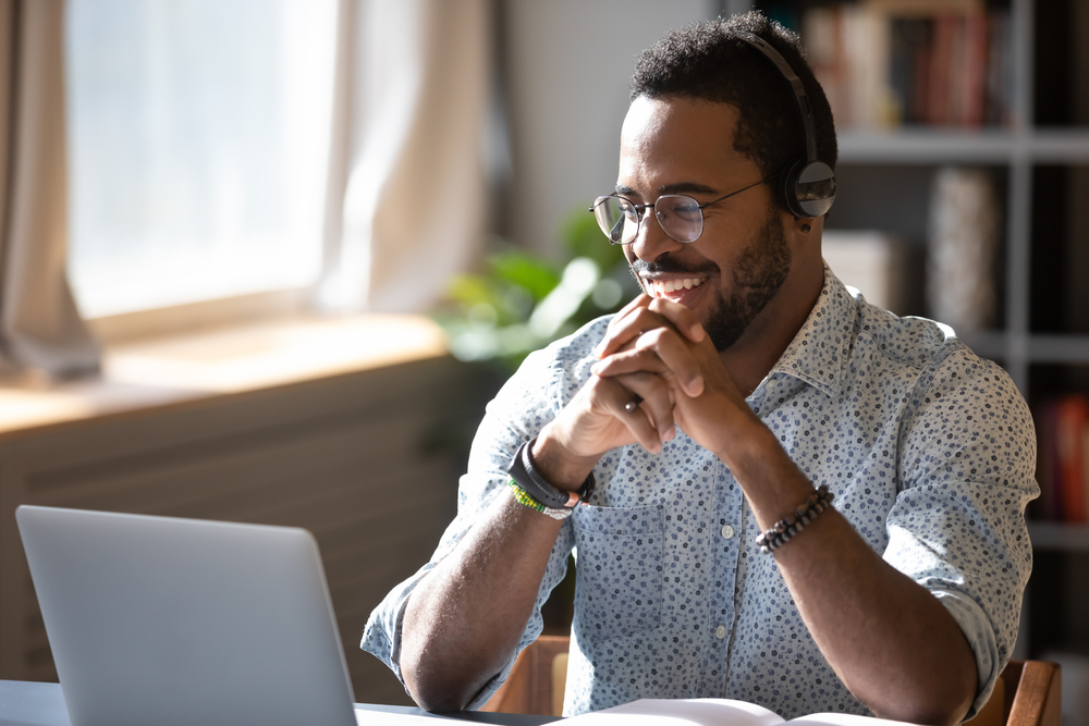 Secrets to Landing Your Dream Remote Job: Happy freelancer in glasses wearing headphones, enjoying watching educational webinar on laptop.